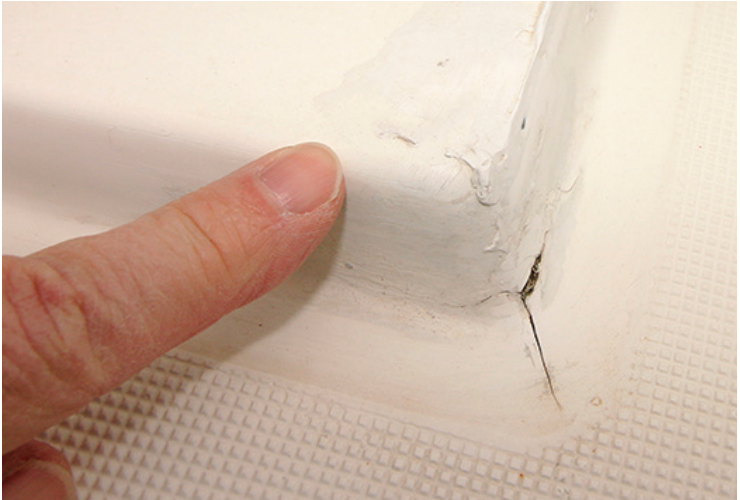 Finger pointing towards a crack in white paint