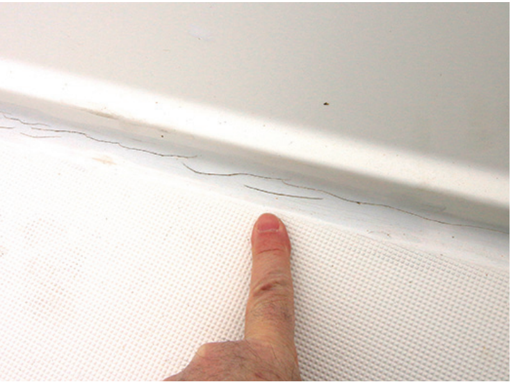 Finger pointing towards a long crack in white gelcoat