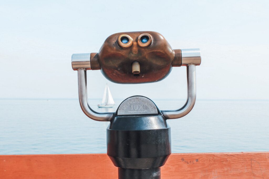 Binoculars attached to a pier, a sail boat in the distance